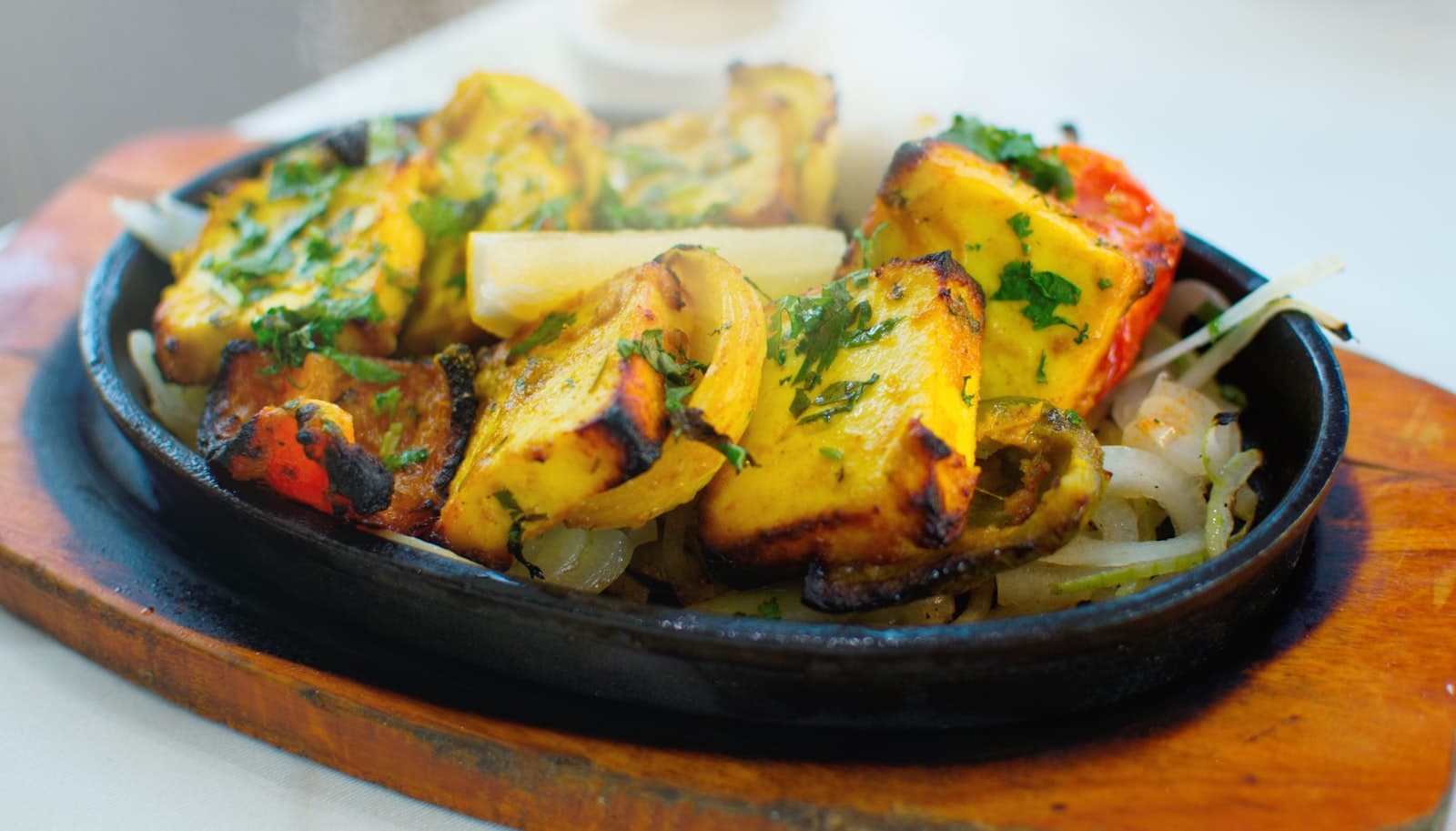 A sizzling cast-iron platter of grilled paneer tikka with onions and peppers